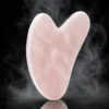 Gua sha en quartz rose – fond noir Gua sha en quartz rose poli sur fond noir avec légère fumée