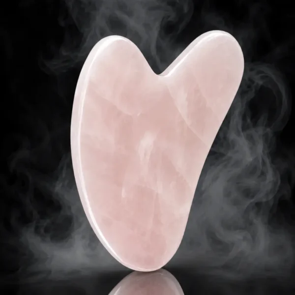 Gua sha en quartz rose – fond noir Gua sha en quartz rose poli sur fond noir avec légère fumée