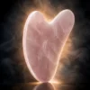 Gua sha en quartz rose – halo lumineux Gua sha en quartz rose sur fond noir avec halo lumineux doux