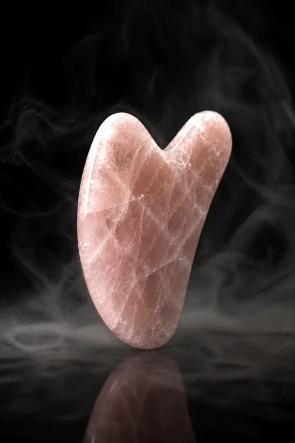 Gua sha en quartz rose avec détails de la pierre naturelle sur fond sombre