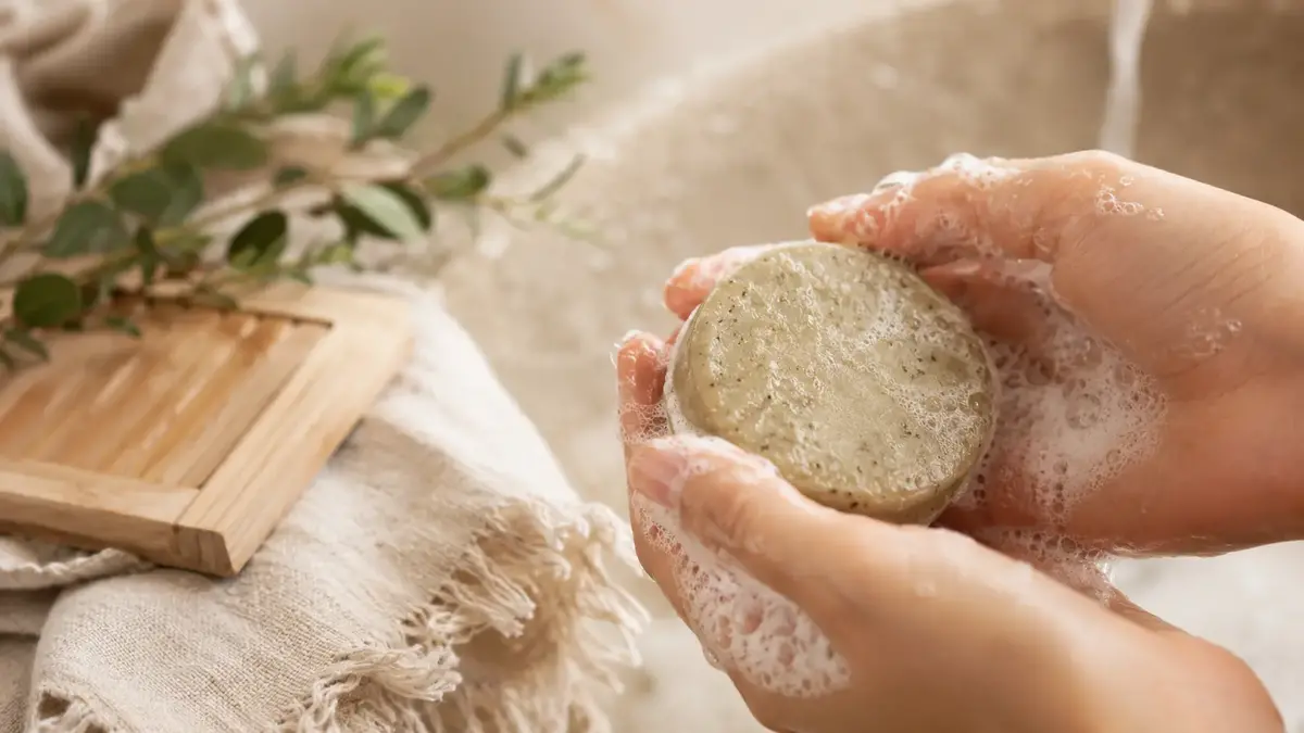 Mains faisant mousser un shampoing solide naturel sous l’eau